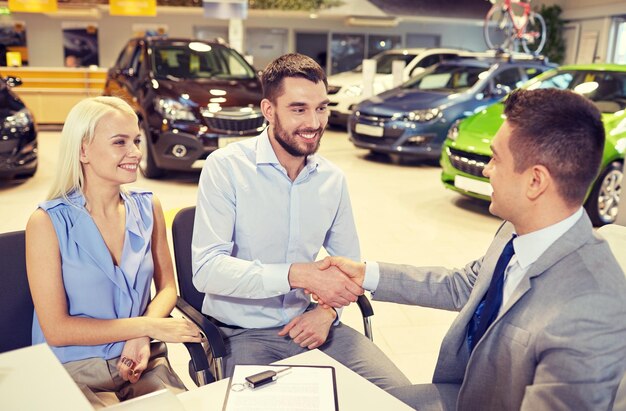 写真 自動車ビジネス、自動車販売、そして人々の概念-自動車ショーやサロンで握手するディーラーとの幸せなカップル