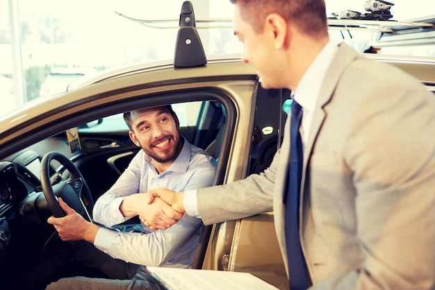 auto business, car sale, consumerism, gesture and people concept - happy man with car dealer making deal and shaking hands in auto show or salon