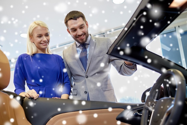 Foto business automobilistico, vendita di auto, consumismo e concetto di persone - coppia felice che acquista auto in auto show o salone su effetto neve