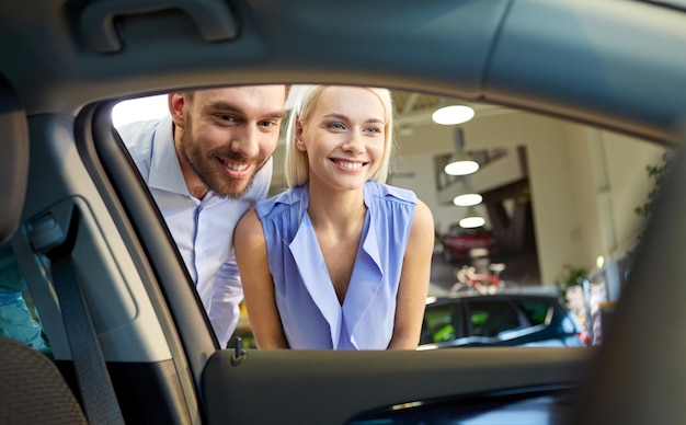 auto business, car sale, consumerism and people concept - happy couple buying car in auto show or salon