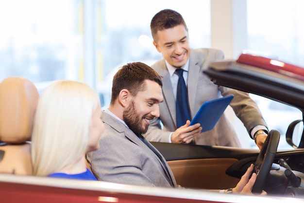 Business automobilistico, vendita di auto, consumismo e concetto di persone - coppia felice con concessionario di auto in auto show o salone