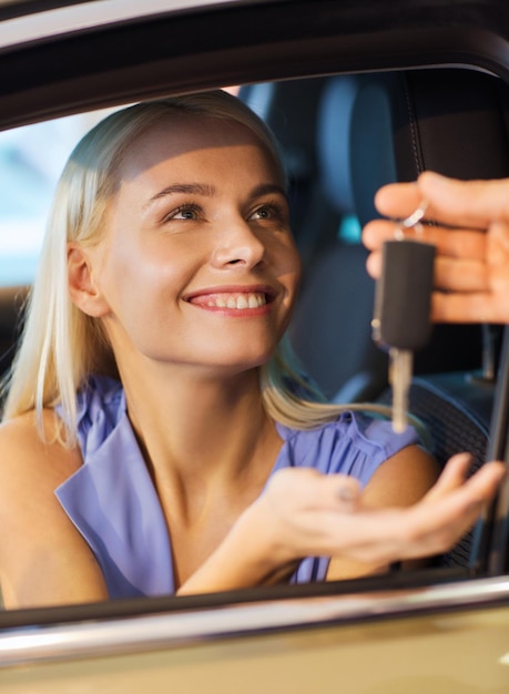 auto business, car sale, consumerism and people concept - happy woman taking car key from dealer in auto show or salon