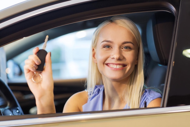 auto business, car sale, consumerism and people concept - happy woman taking car key from dealer in auto show or salon