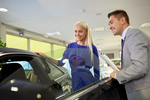 Auto business, car sale, consumerism and people concept - happy\
woman with car dealer in auto show or salon