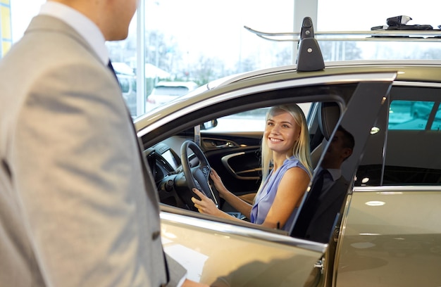 自動車ビジネス、自動車販売、消費主義、人々のコンセプト – 自動車ショーやサロンで車のディーラーを持つ幸せな女性