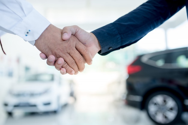 Photo auto business, car sale, deal, gesture and people concept - close up of dealer giving key to new owner and shaking hands in auto show or salon