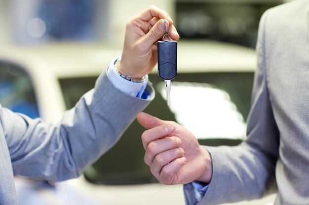 auto business, car sale, deal and people concept - close up of male hands with car key in auto show or salon