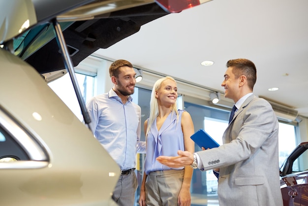 Business automobilistico, vendita di auto, tecnologia e concetto di persone - coppia felice con concessionario di auto in auto show o salone