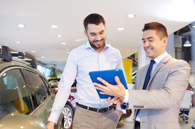 auto business, car sale, technology and people concept - happy man and car dealer with tablet pc computer in auto show or salon