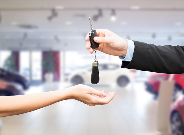 auto business, car sale, transportation, people and ownership concept - close up of car salesman giving key to new owner or customer over auto show background