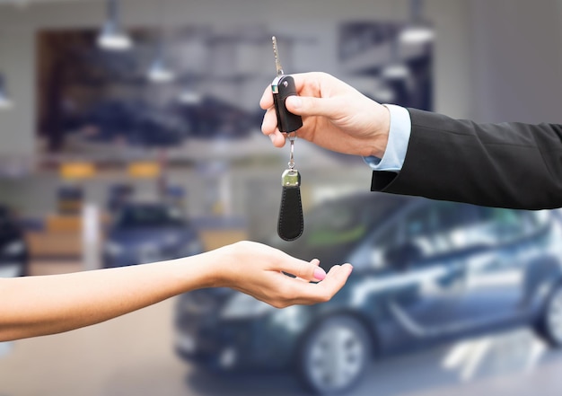 auto business, car sale, transportation, people and ownership concept - close up of car salesman giving key to new owner or customer over auto show background