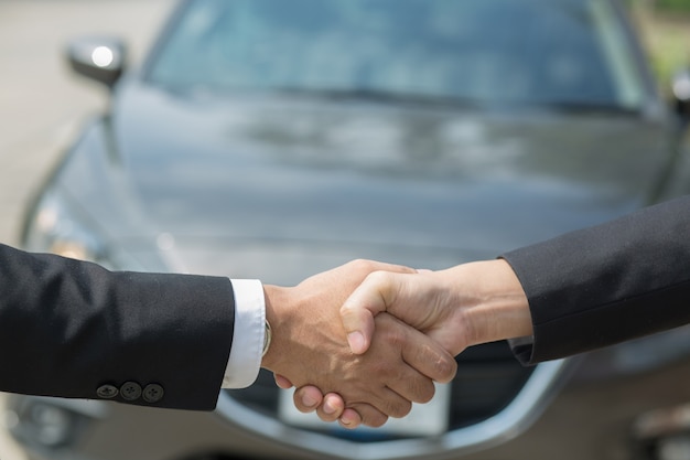 자동차 사업. 새로운 소유자에게 사업가 딜러 제공 자동차의 닫고 고객에게 두 축하 사이의 손을 흔들어. 아침에 맑은 야외 필터 톤.