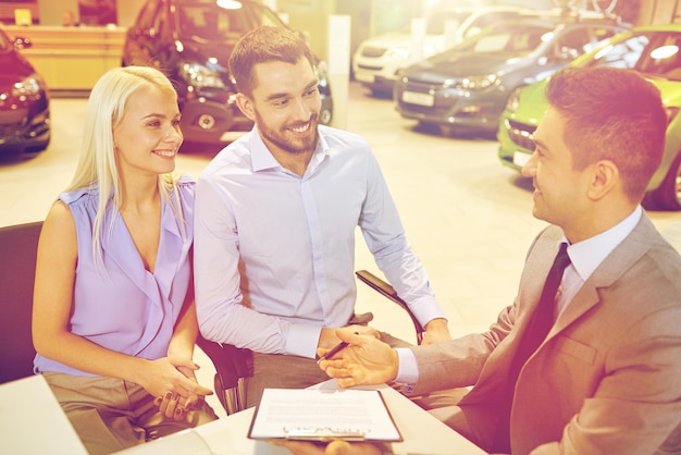 Auto business, sale and people concept - happy couple with dealer buying car in auto show or salon