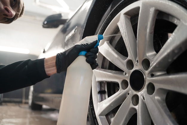 Auto detailing worker applies chemistry to wheels.