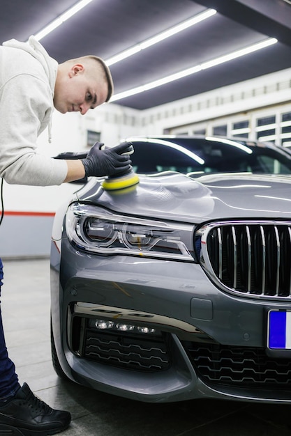 Auto detaillering - werknemer met orbitale polijstmachine in auto reparatiewerkplaats.