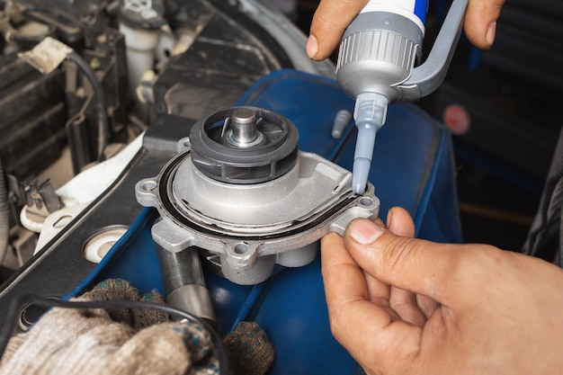 An auto mechanic applies silicone black sealant to a new engine cooling pump before installing it