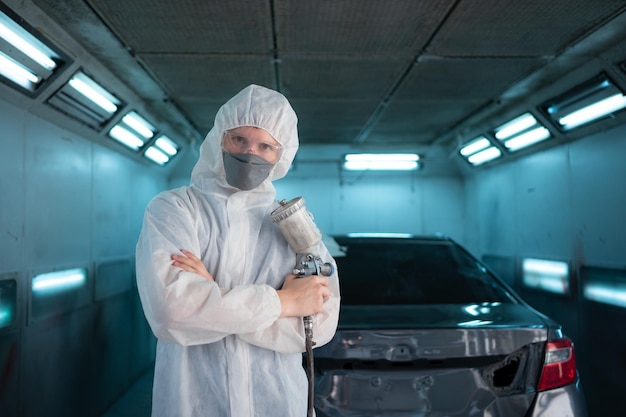 Auto mechanic in car spray room giving the spray nozzle injected into the car front bumper of car