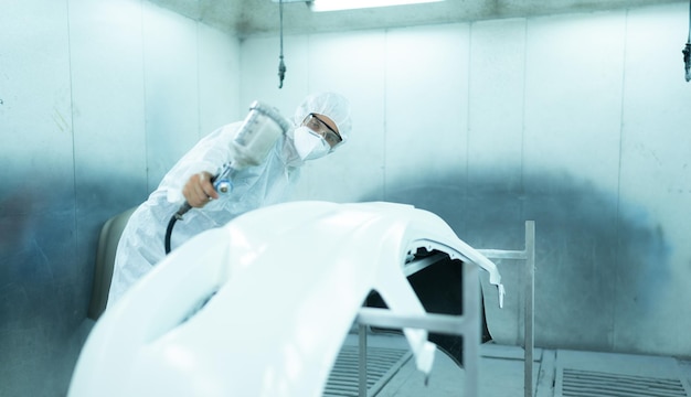 Auto mechanic in car spray room giving the spray nozzle injected into the car front bumper of car