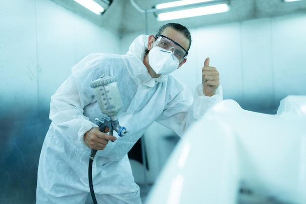 Auto mechanic in car spray room giving the spray nozzle injected into the car front bumper of car