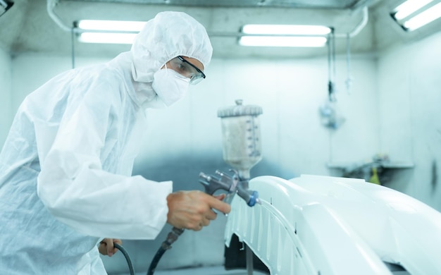 Auto mechanic in car spray room giving the spray nozzle injected into the car front bumper of car