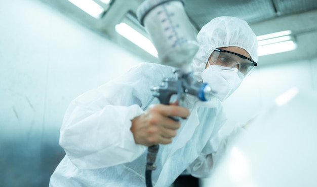 Auto mechanic in car spray room giving the spray nozzle injected into the car front bumper of car