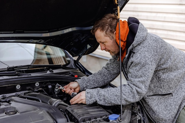 Auto mechanic caucasian white man working in a car repair shop\
installing the new battery under the hood