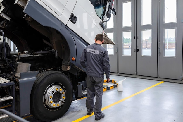 Foto meccanico automobilistico che controlla il camion nel garage che fa la manutenzione e la riparazione dei camion in un grande garage