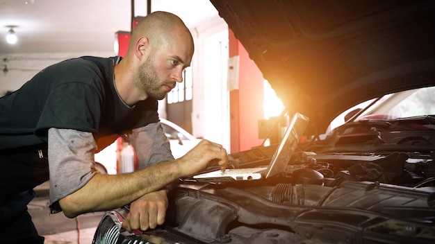 Il meccanico automatico diagnostica un'auto utilizzando un primo piano dell'officina dell'auto del computer