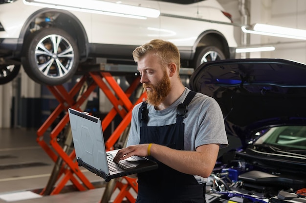 An auto mechanic engineer stands with a professional diagnostic laptop against the background of a service station Diagnosis of vehicle errors