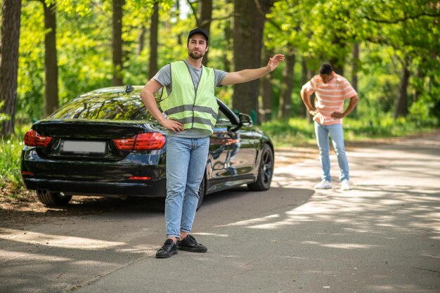 緑のベストを着た自動車整備士が林道でヒッチハイク