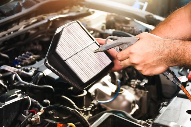 Foto la mano del meccanico automatico sta soffiando polvere e pulendo un filtro dell'aria per auto con una pistola ad aria compressa