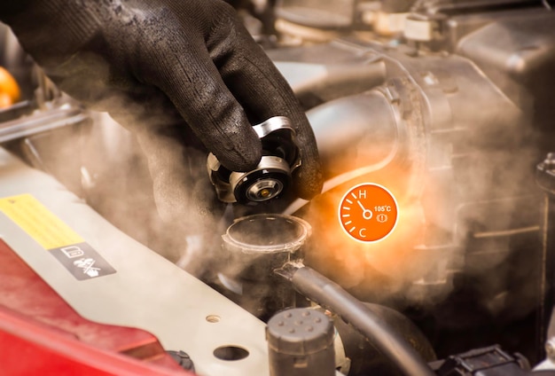 Auto mechanic hand opens the radiator cap with steam escaping around the engine compartment from the high heatwater temp gauge symbol with high temperatureCar maintenance service concept