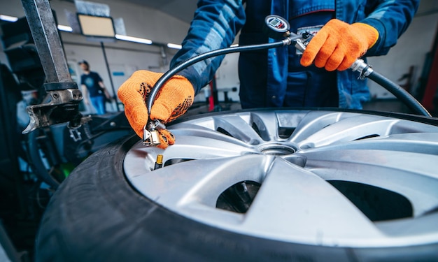 Meccanico automobilistico che effettua il controllo della pressione dei pneumatici dell'auto sulla ruota rimossa nel garage di servizio automatico