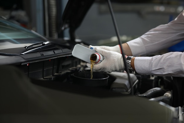 Автомеханик наливает масло в двигатель из банок с маслом.