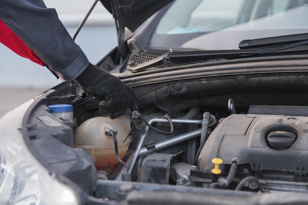 Auto mechanic unscrews expansion tank cap to pour antifreeze in car service workshop