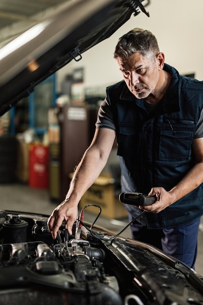 Auto mechanic using diagnostic tool while checking car battery in repair workshop