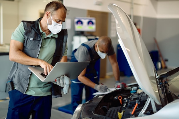 Foto meccanico automatico che utilizza il laptop durante l'esecuzione della diagnostica del motore con il suo collega in officina