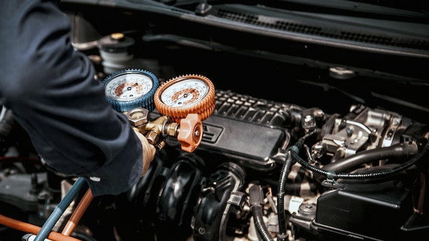 Auto mechanic using measuring equipment tool for filling car air conditioners.