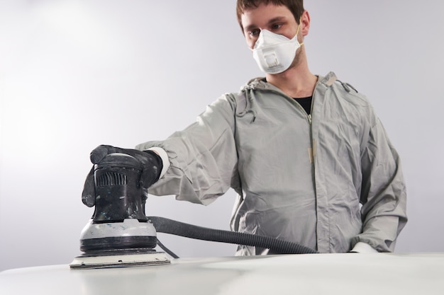 Auto mechanic wearing face mask buffing and polishing car hood in auto repair shop