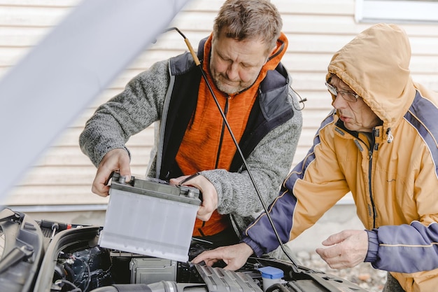 Auto mechanics Caucasian White mans working in a car repair shop Installing the new battery under the hood