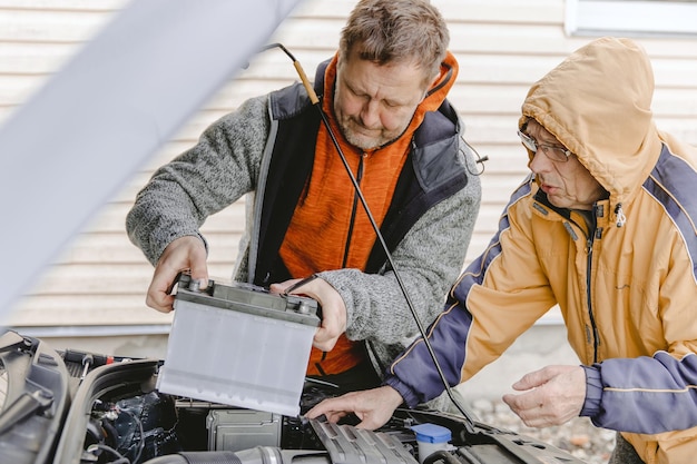 Auto mechanics caucasian white mans working in a car repair\
shop installing the new battery under the hood