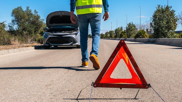 Auto met problemen en man zet een rode driehoek om andere weggebruikers te waarschuwen Mannelijke bestuurder staat in de buurt van een kapotte auto met open kap wachten op hulp