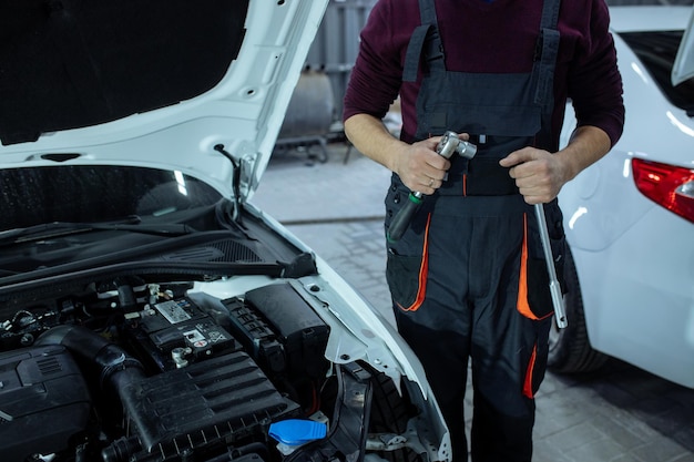 Auto onderhoud. Een automonteur staat bij de auto met een gereedschap in zijn handen. Technische keuring van het voertuig.