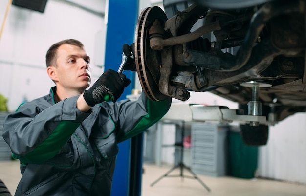 Auto opgetild in autoservice voor reparatie, werknemer repareert het wiel,