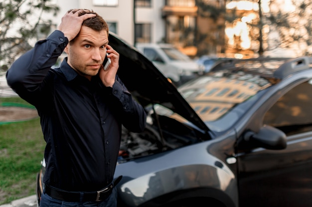 Auto pech concept. De auto start niet. Een jonge man roept om een autoservice. Ze kunnen de auto niet zelf repareren. De verzekering moet alle kosten dekken.