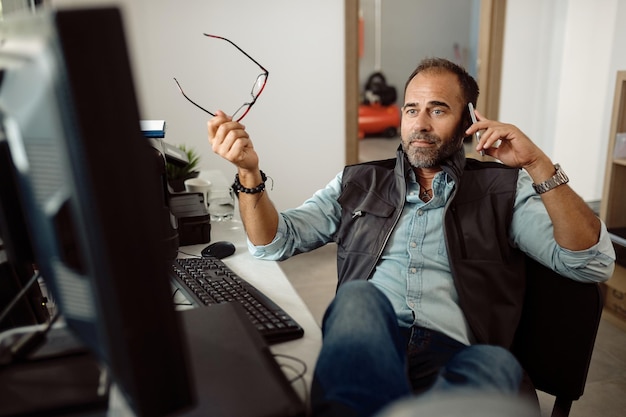 Auto repairman talking on mobile phone while using computer at\
workshop\'s office