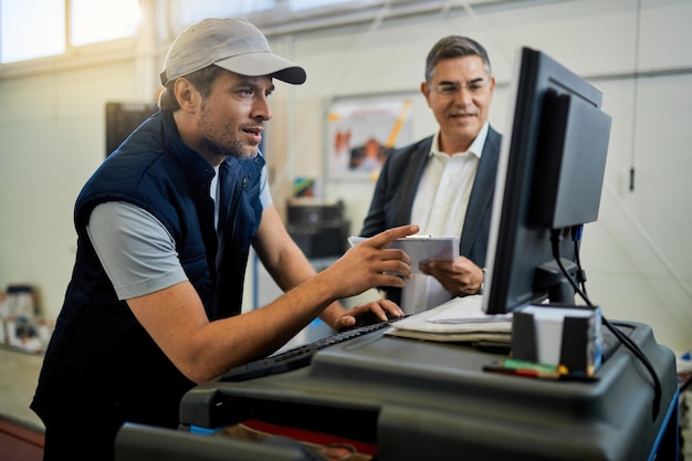 Auto repairman working on computer while talking with his manager in a workshop