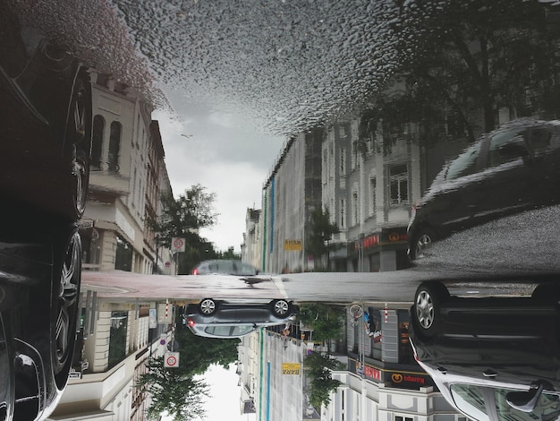 Auto's en gebouwen die zich weerspiegelen in een plas op een stadsstraat