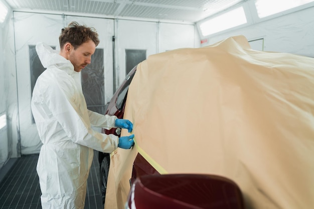 Auto schilder maskeert auto met papier voor het schilderen of polijsten in de spuitcabine