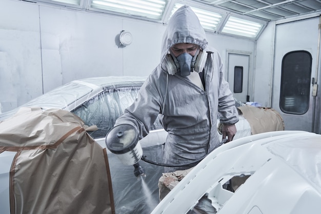 Auto schilderen en auto reparatie service. Automonteur in witte overall schildert auto met airbrush-pulverizer in verfkamer